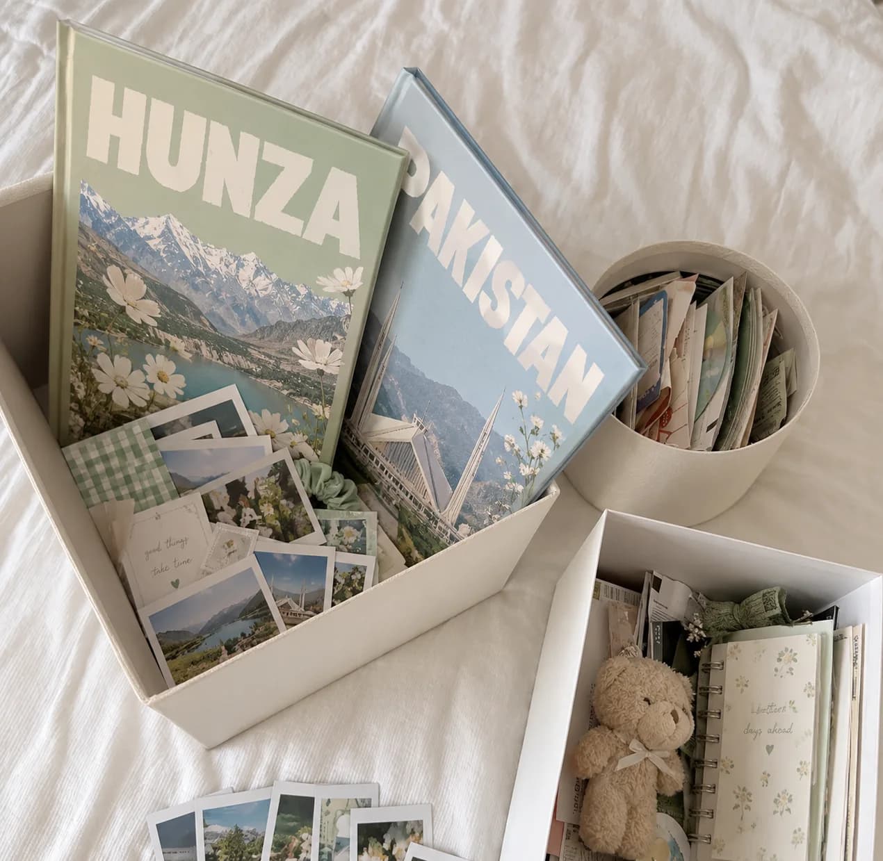 Two Pixorh photobooks, Hunza and Pakistan, in an open box with prints, a teddy and a notebook beside them