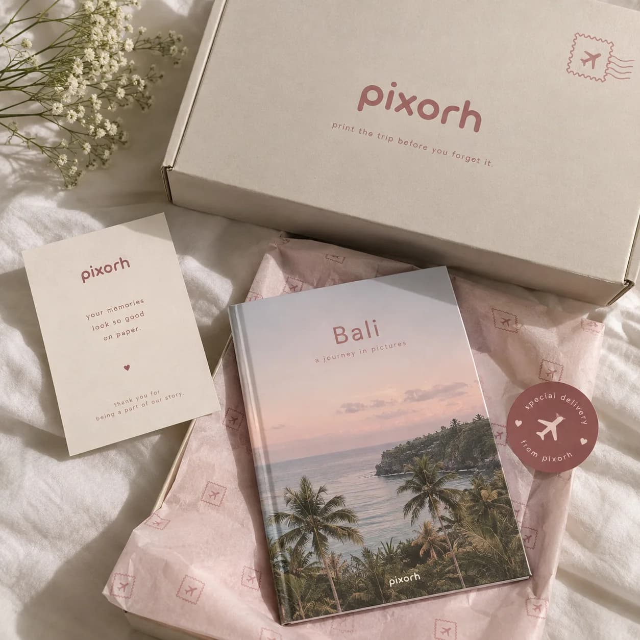 A Pixorh mailer box with a thank-you card, pink tissue paper and a Bali photobook